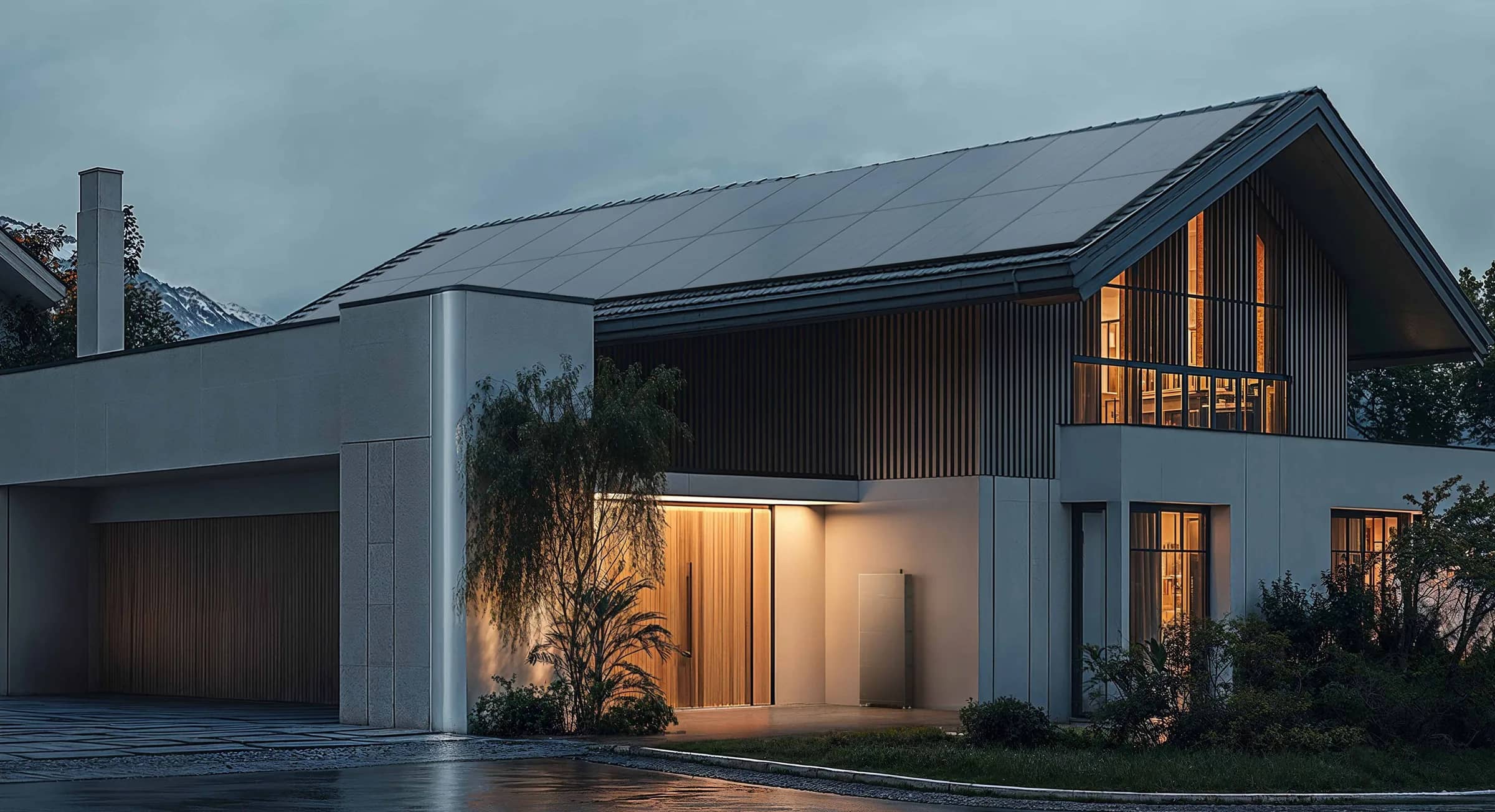 A home battery on the outside wall of a house at dusk, with the windows lit