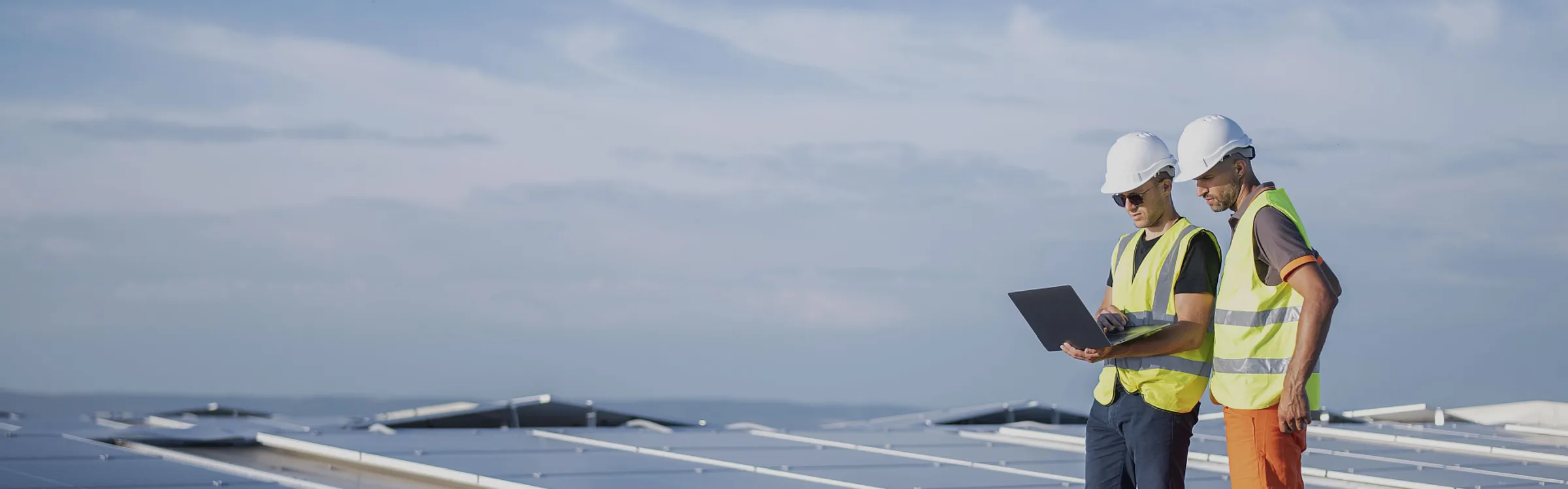 An engineer in a hard hat and hi-vis on a flat commercial roof covered in solar panels