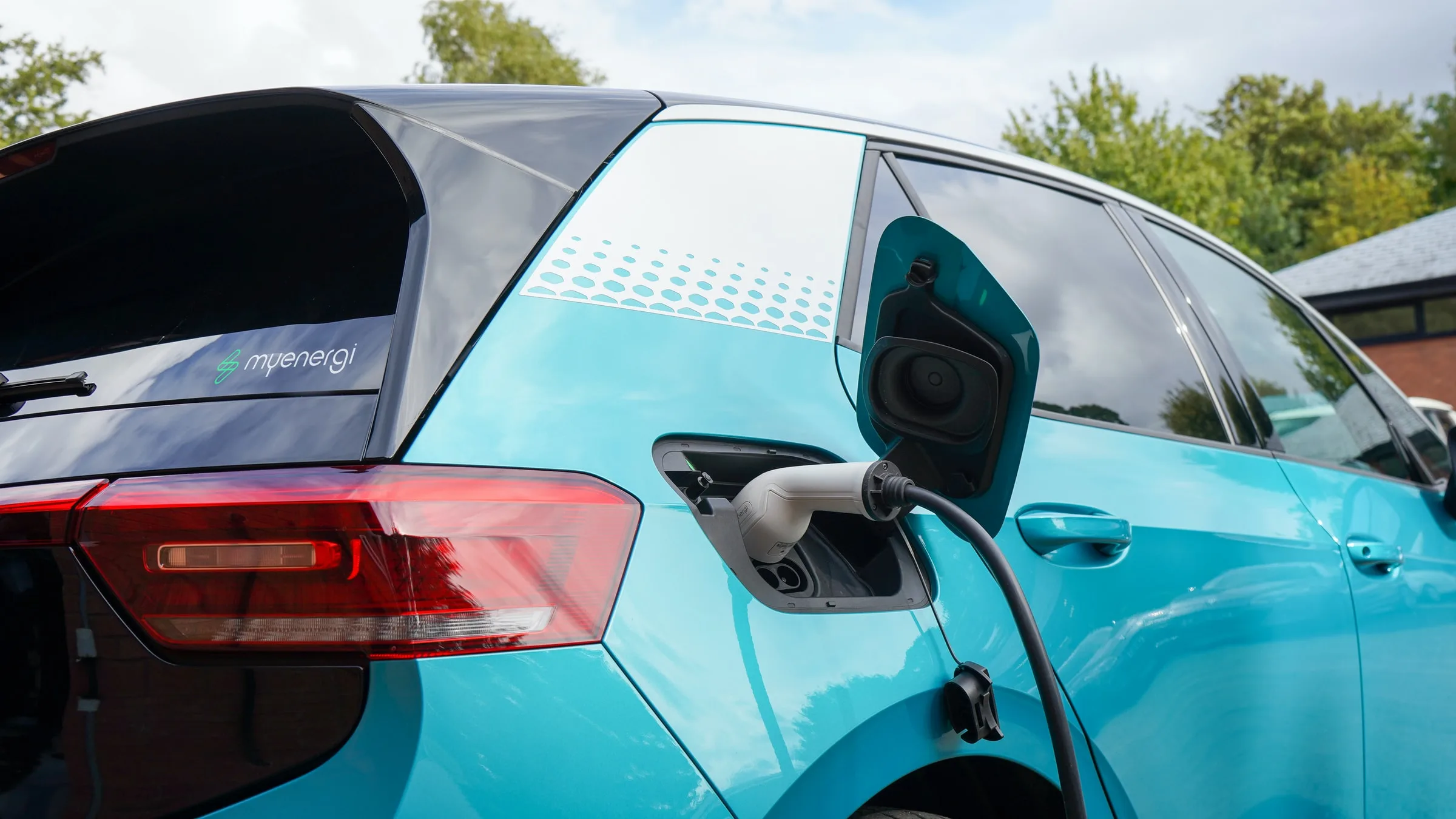 A teal electric car plugged in and charging on a home drive on a bright day